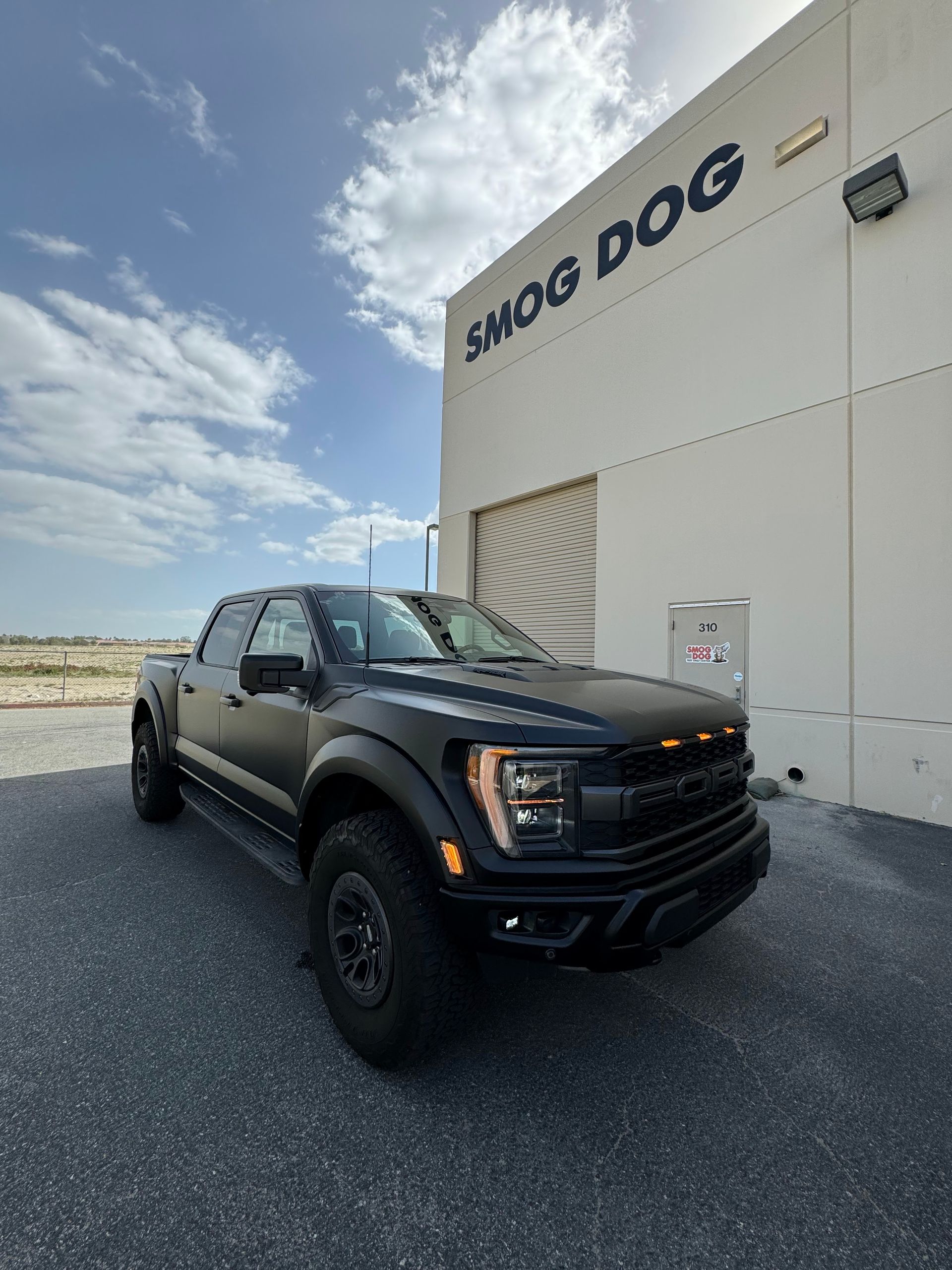 A black truck is parked in front of a building that says smog dog.