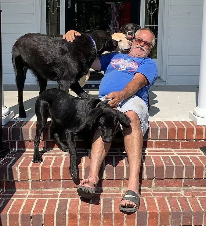 Man sitting on brick steps surrounded by four dogs; one being petted.