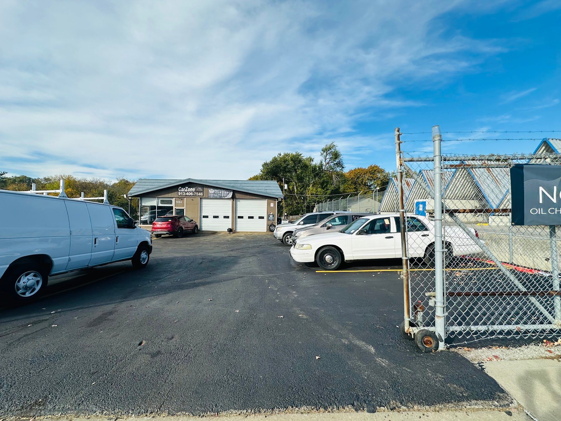 Parking lot with vehicles in front of a building with garage doors, under a blue sky | Automotive Concierge KC
