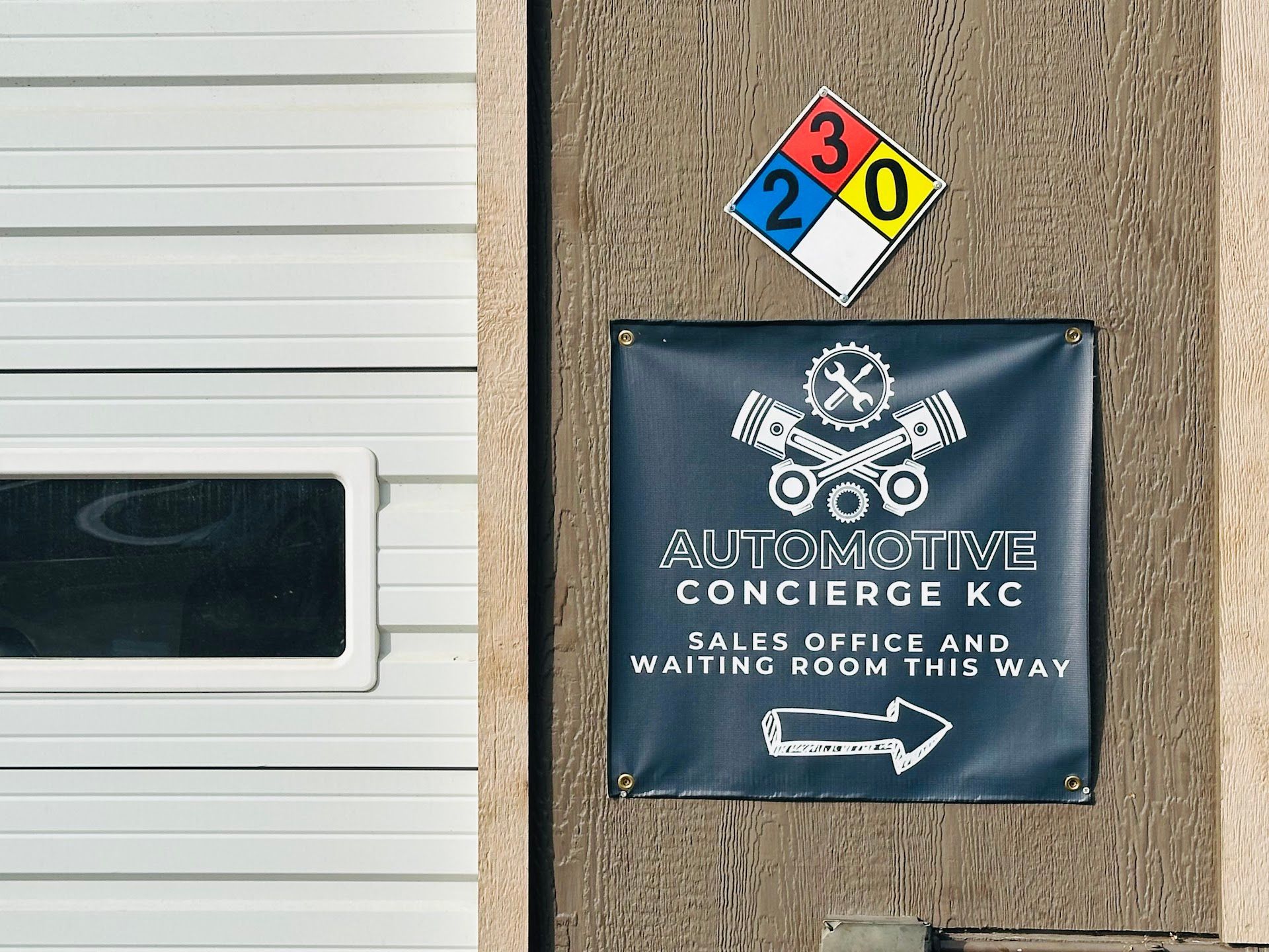 Automotive Concierge KC sign with hazard diamond, pointing to sales office. White garage door in background | Automotive Concierge KC