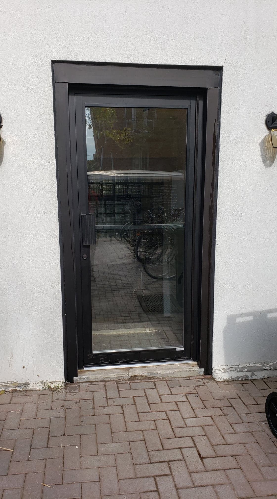 A black door is sitting on a brick patio next to a white wall.
