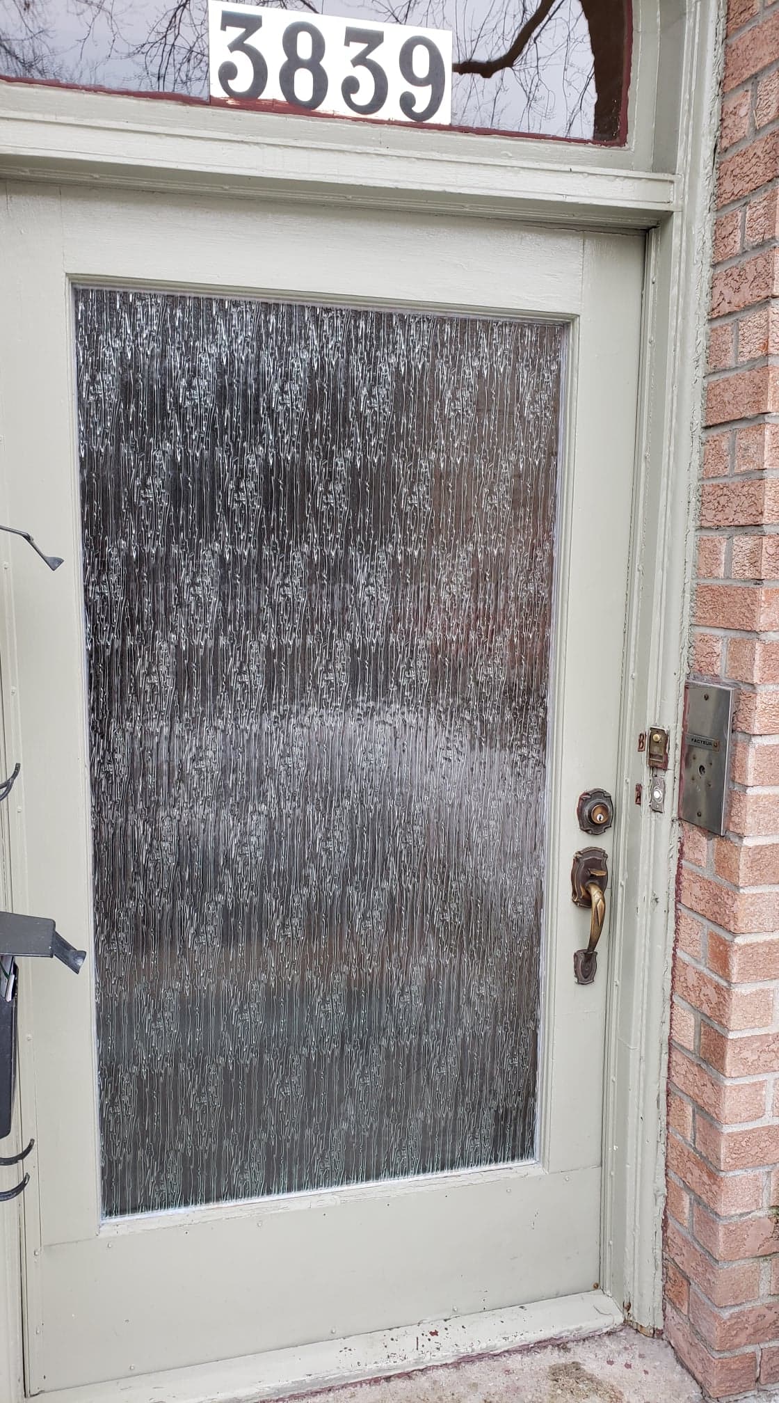 A white door with a clear glass window is on a brick wall.