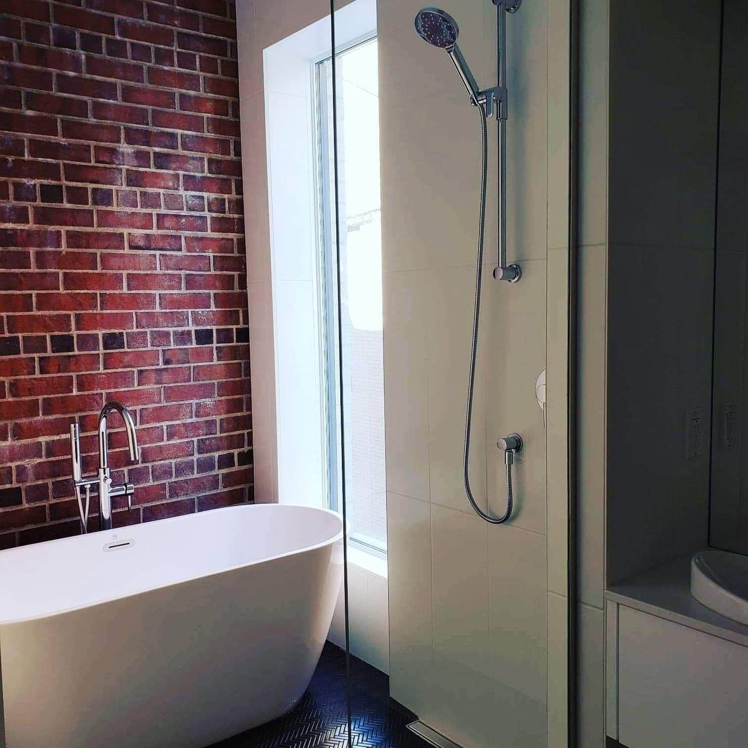 Une salle de bain avec une baignoire et une douche avec un mur de briques