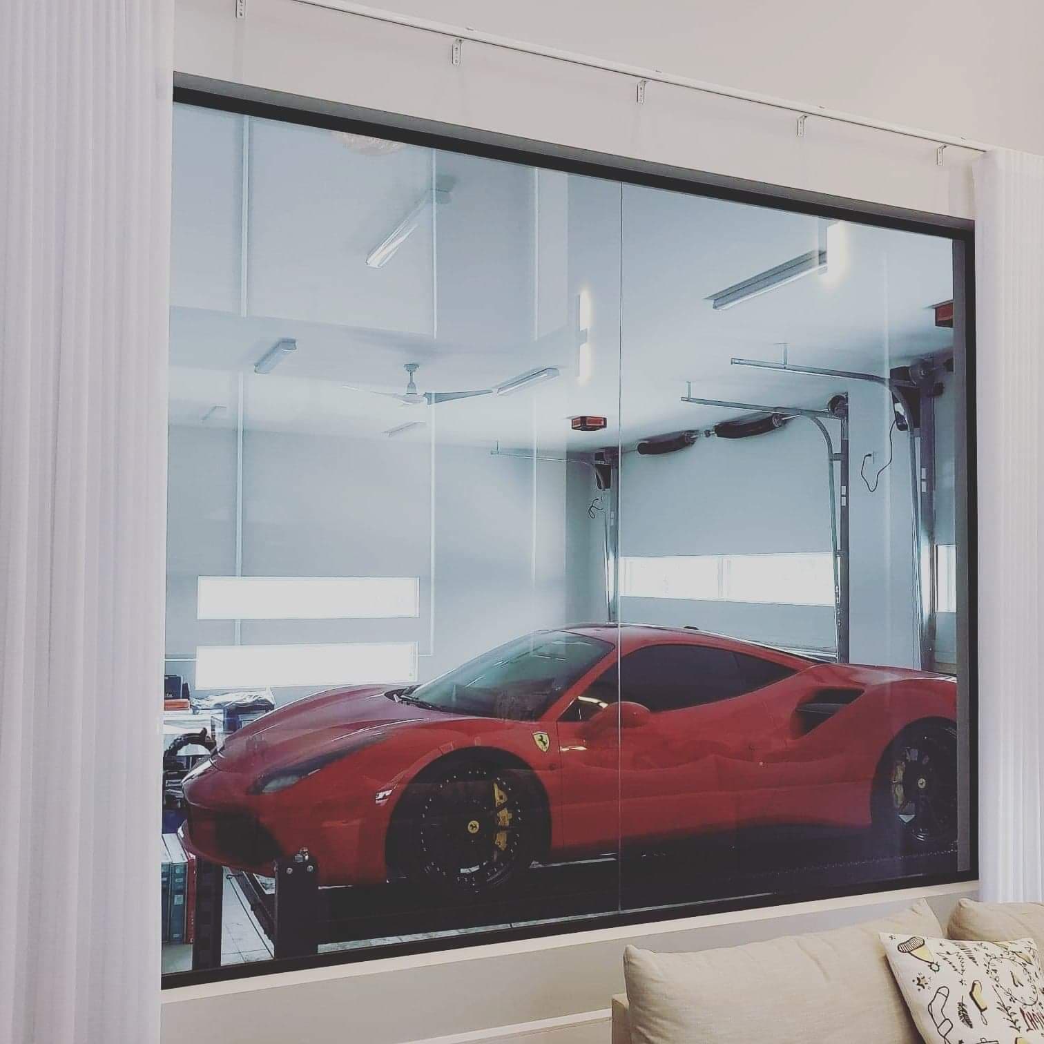 Une voiture de sport rouge est garée dans un garage à travers une fenêtre