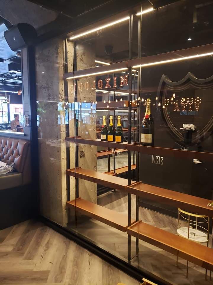 Une pièce avec un mur en verre et des étagères remplies de bouteilles de champagne.