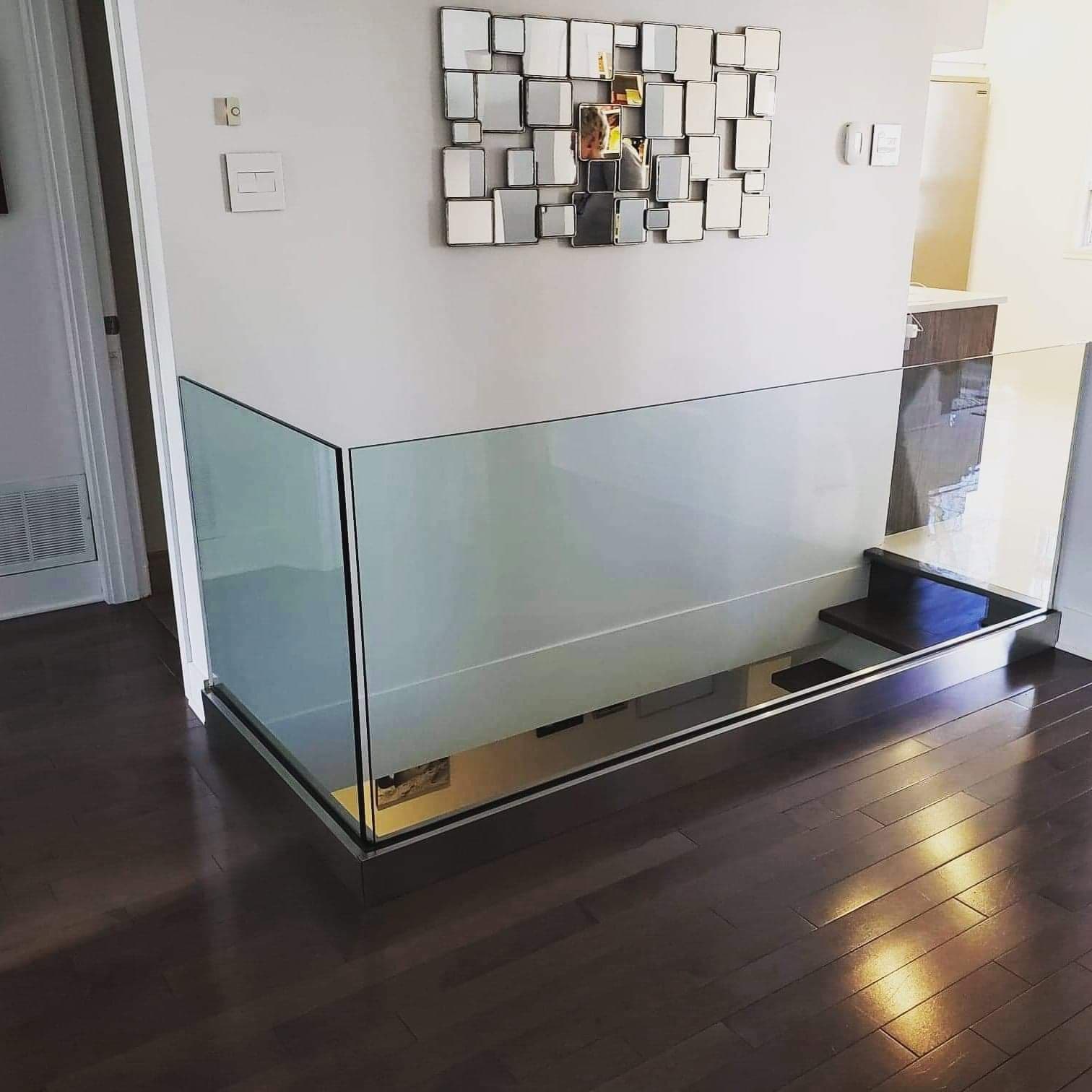 Un escalier avec une rampe en verre et un miroir au mur.