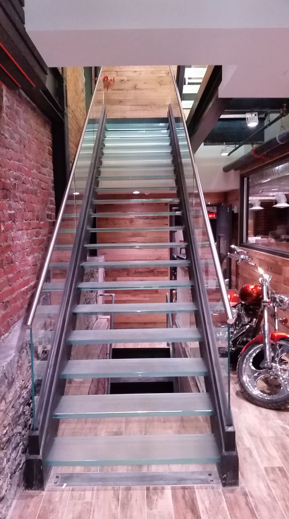 Un escalier avec une rampe en verre et une moto en arrière-plan.