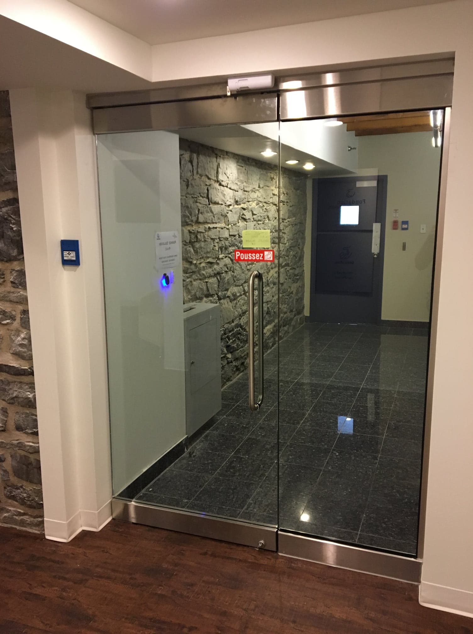 Une porte vitrée avec un cadre en acier inoxydable est ouverte dans un couloir.