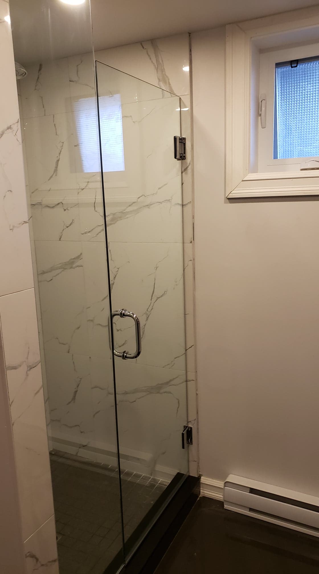 Une salle de bain avec une porte de douche en verre et une fenêtre.
