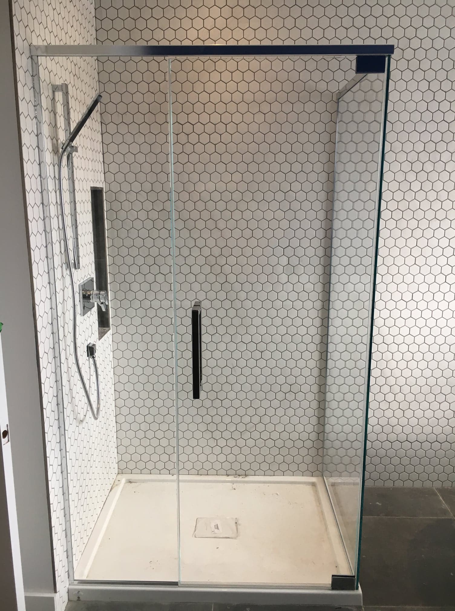 Une cabine de douche avec une porte vitrée et du carrelage blanc sur le mur.
