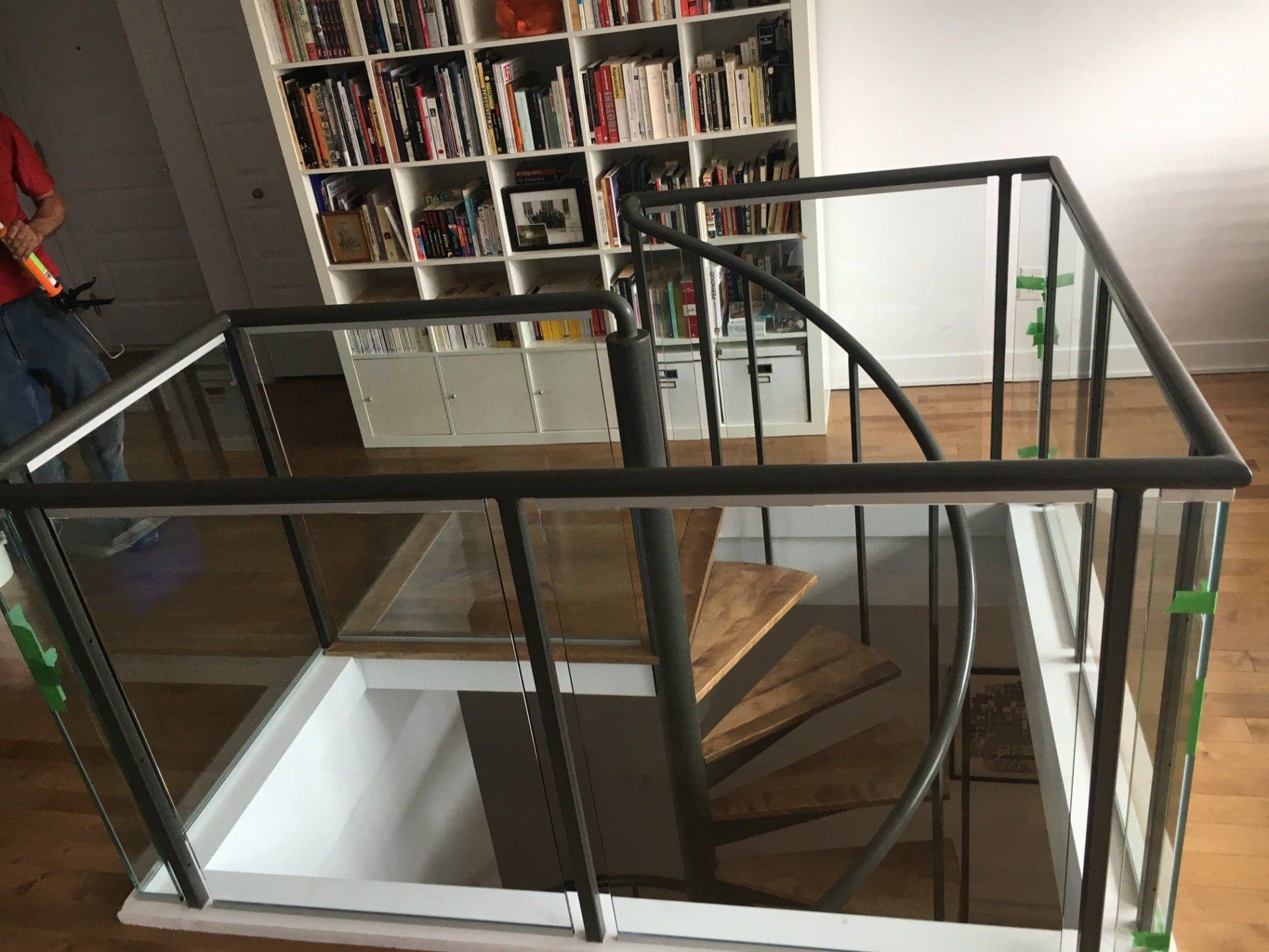 Un escalier en colimaçon avec une rampe en verre et une étagère en arrière-plan.