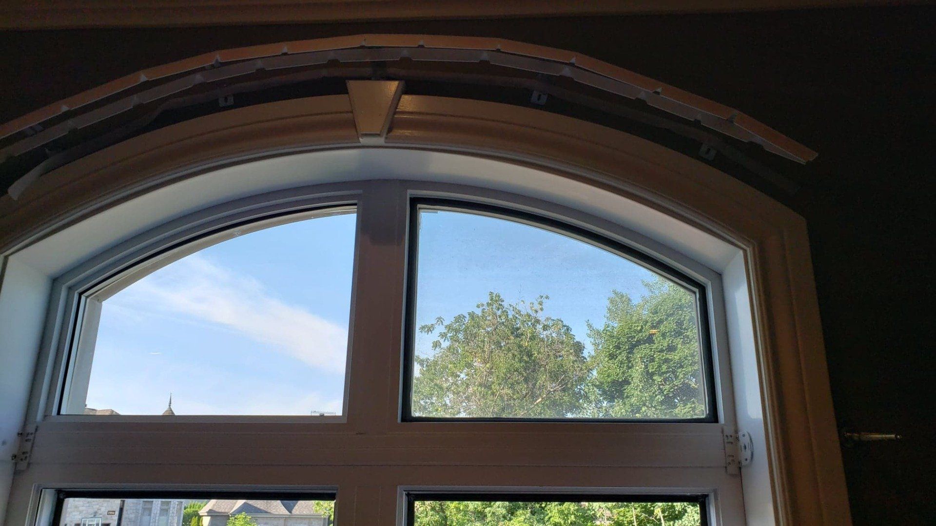 Une grande fenêtre cintrée avec vue sur les arbres et un ciel bleu.