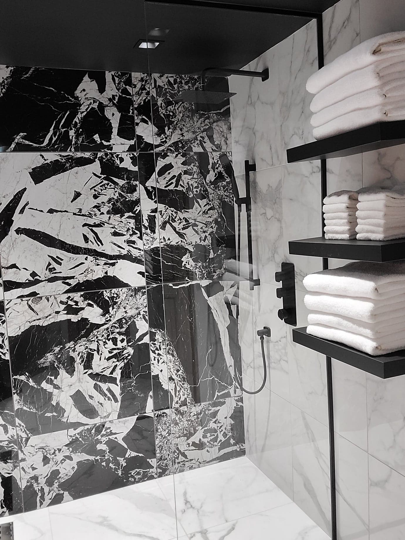 Une photo en noir et blanc d'une salle de bain avec douche et serviettes sur des étagères.