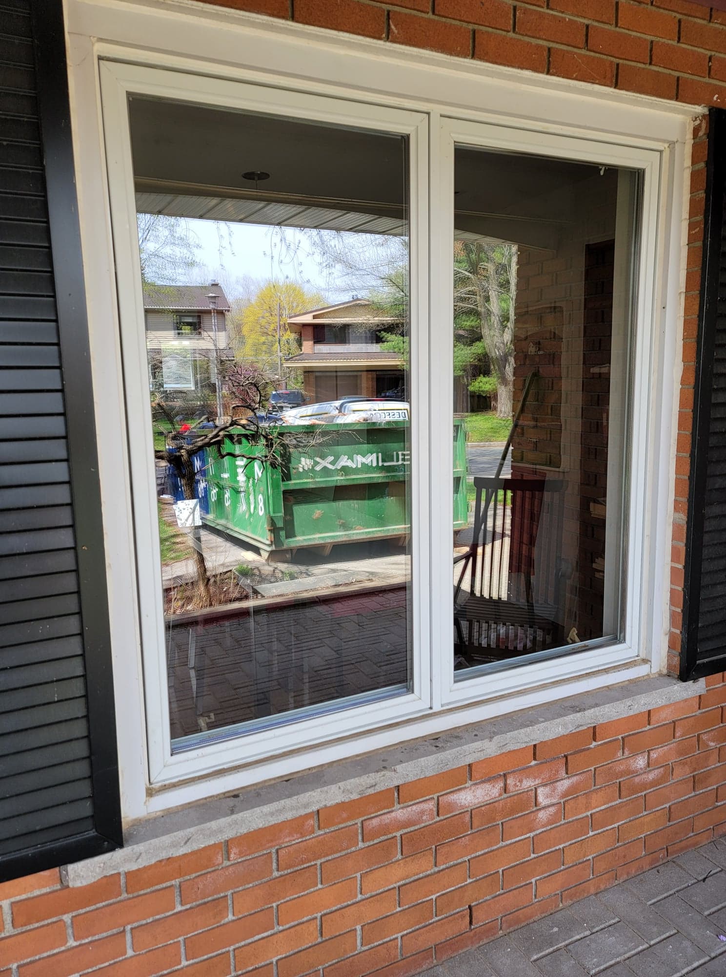 Une fenêtre blanche sur un mur de briques avec des volets noirs.