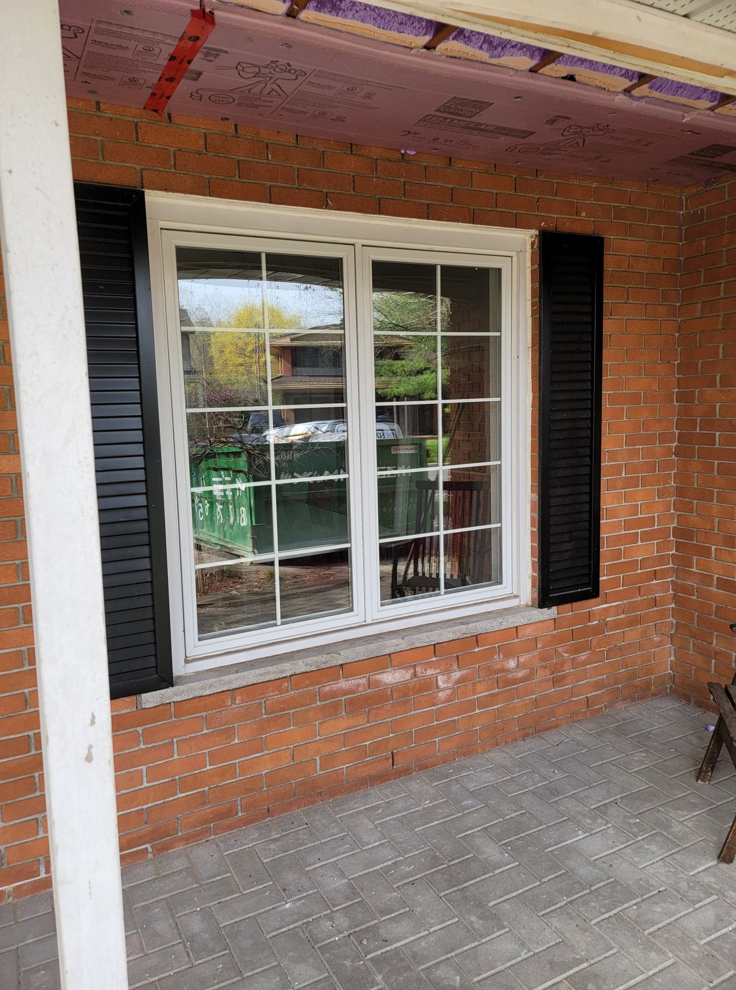 Une fenêtre blanche avec des volets noirs sur un mur de briques.
