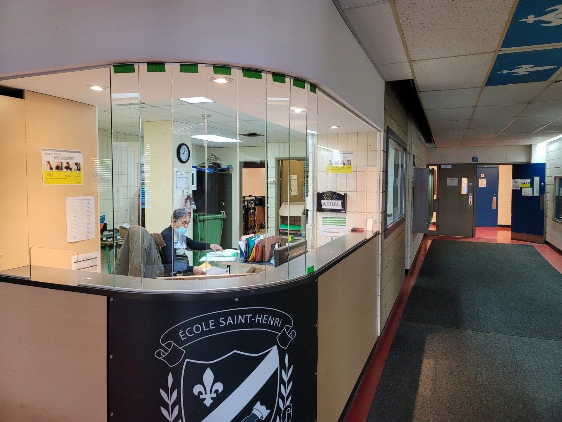 Un homme portant un masque est assis à un bureau dans un couloir.