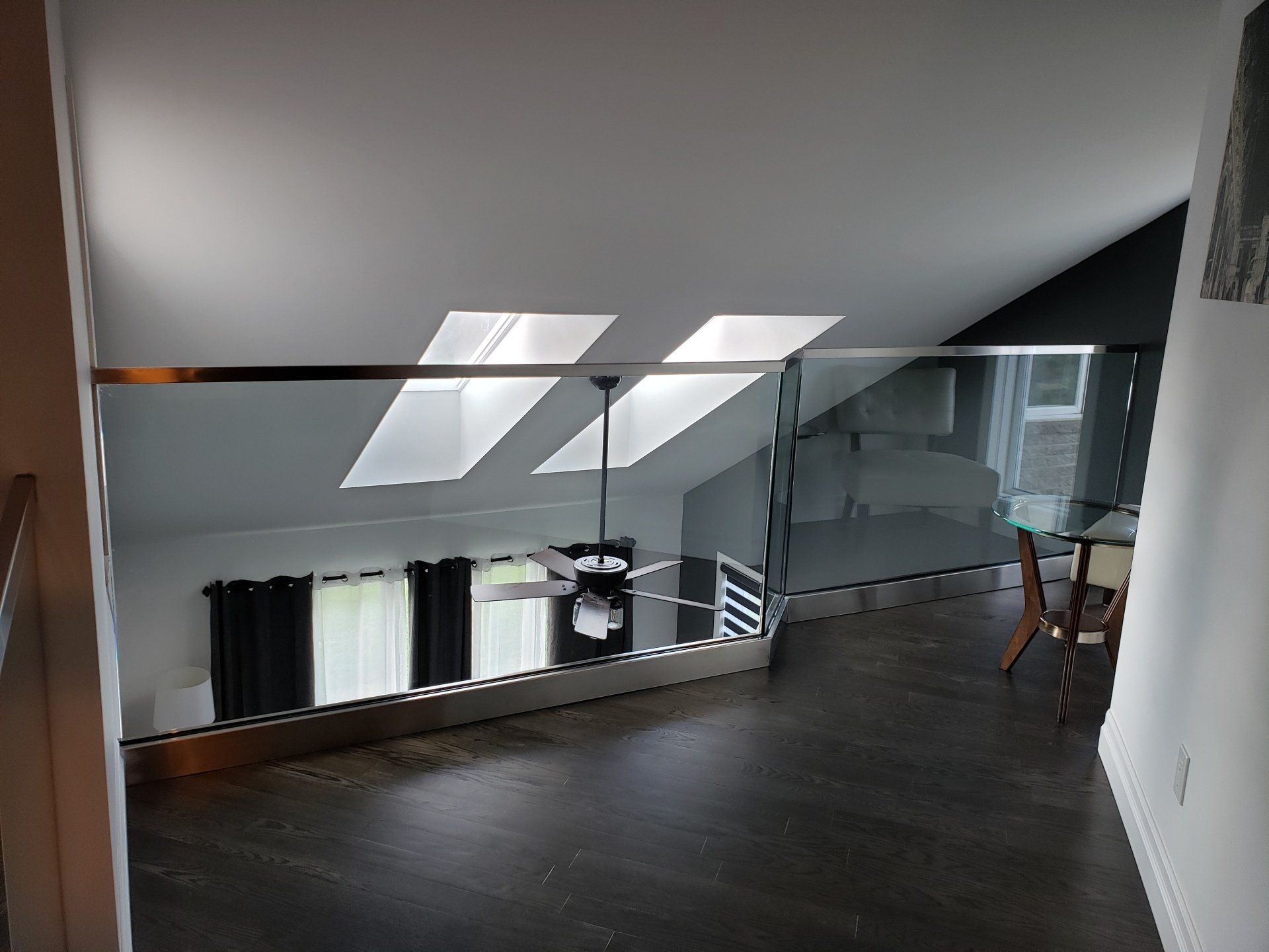 Un couloir avec une balustrade en verre et un ventilateur de plafond