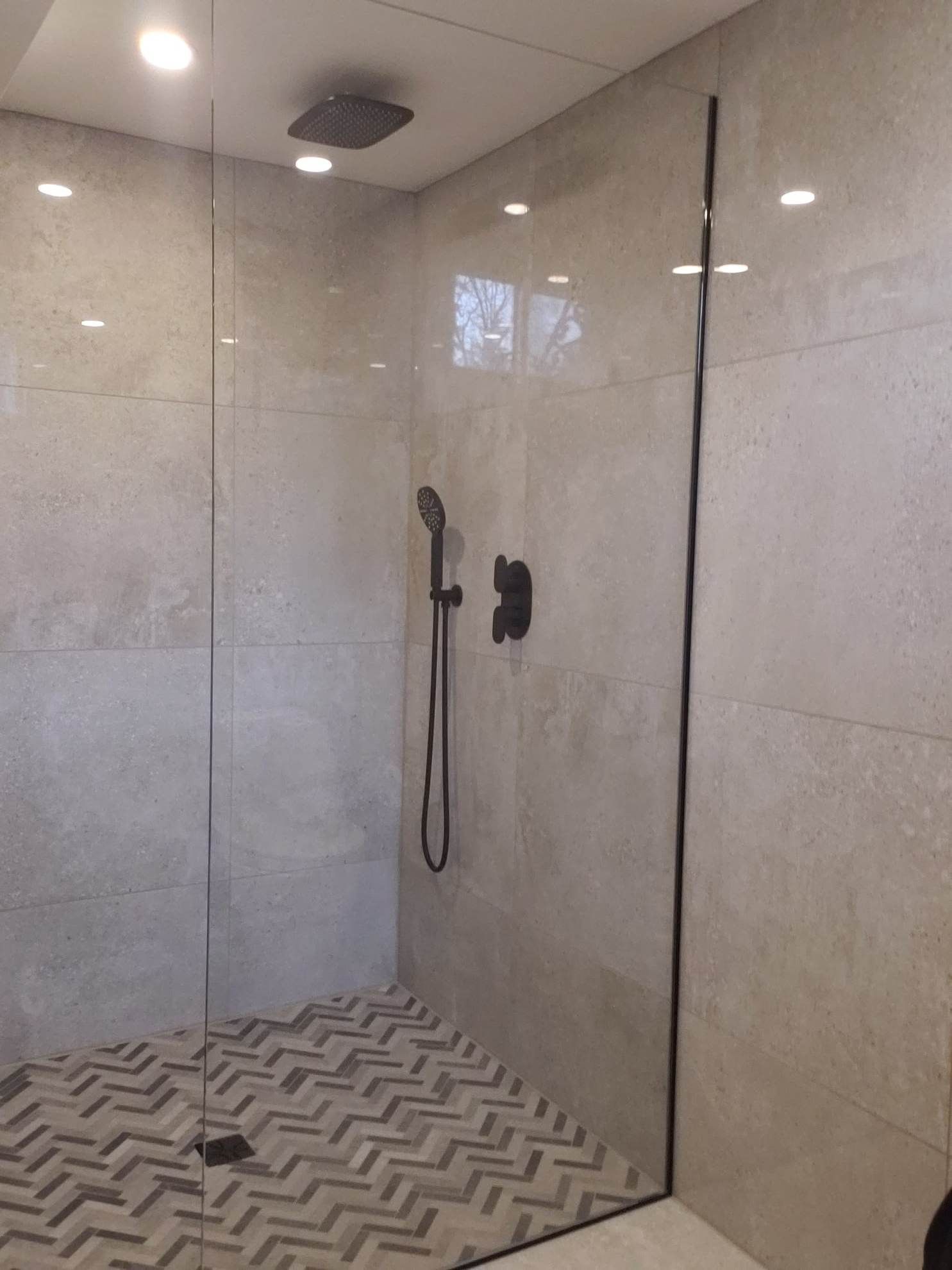 Une douche à l'italienne avec une porte en verre et une pomme de douche noire.