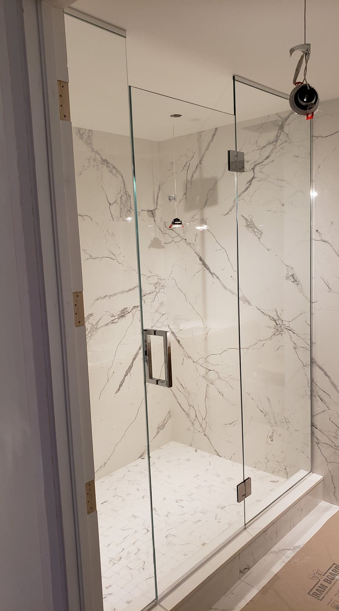 Une cabine de douche avec une porte vitrée dans une salle de bain aux murs en marbre.