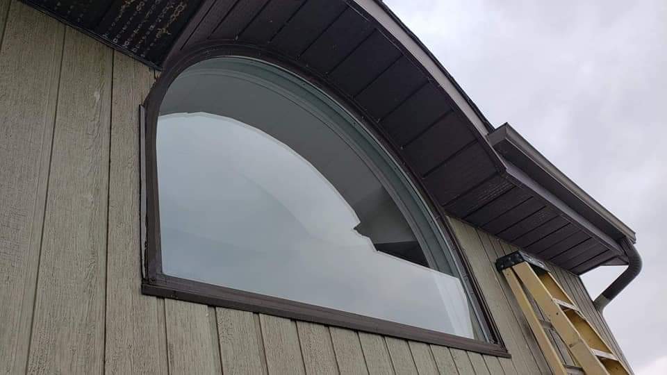 Une grande fenêtre courbée sur le côté d'une maison avec une échelle attachée à elle.