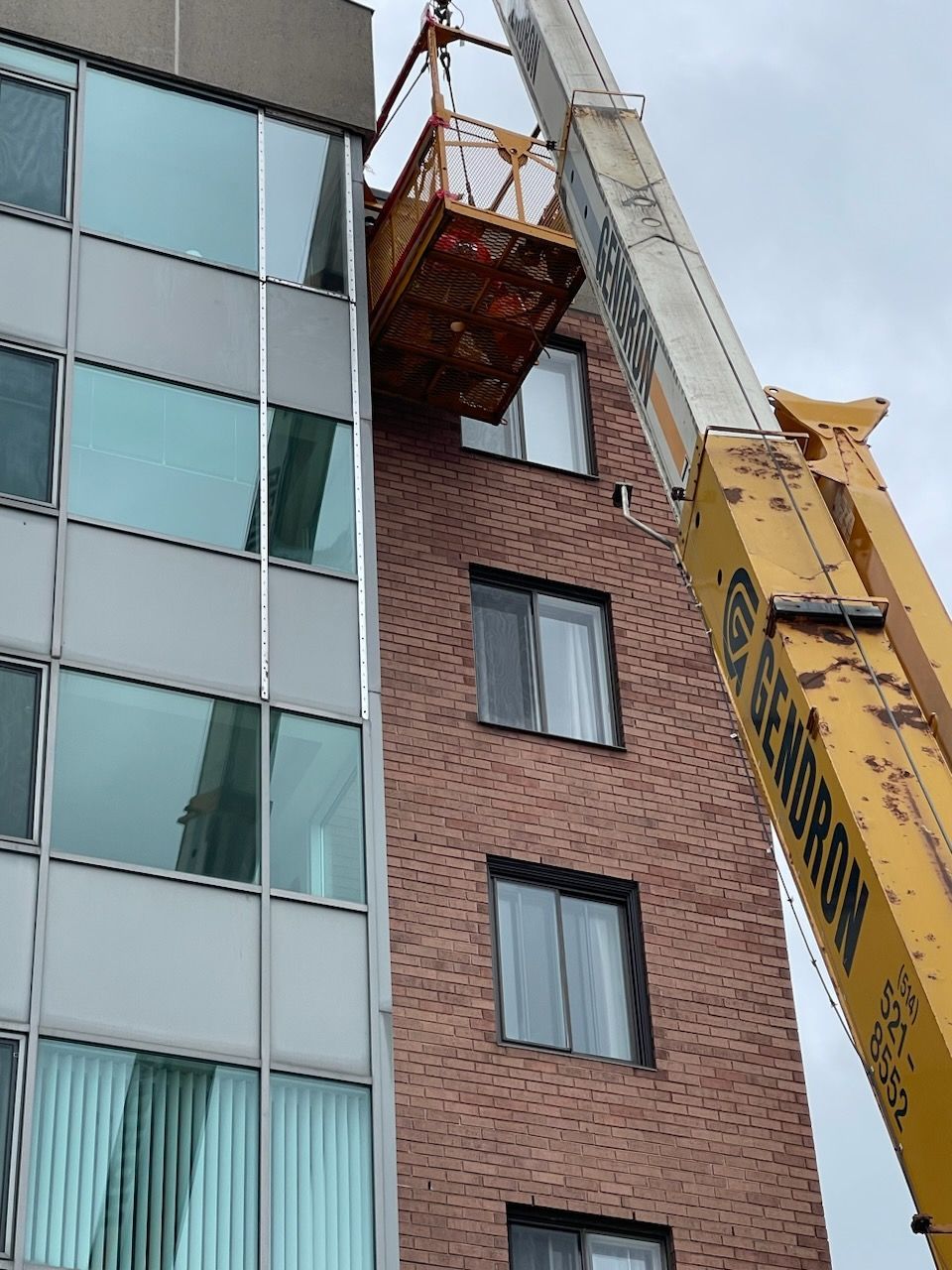 Une grue jaune est attachée au côté d'un bâtiment en briques.