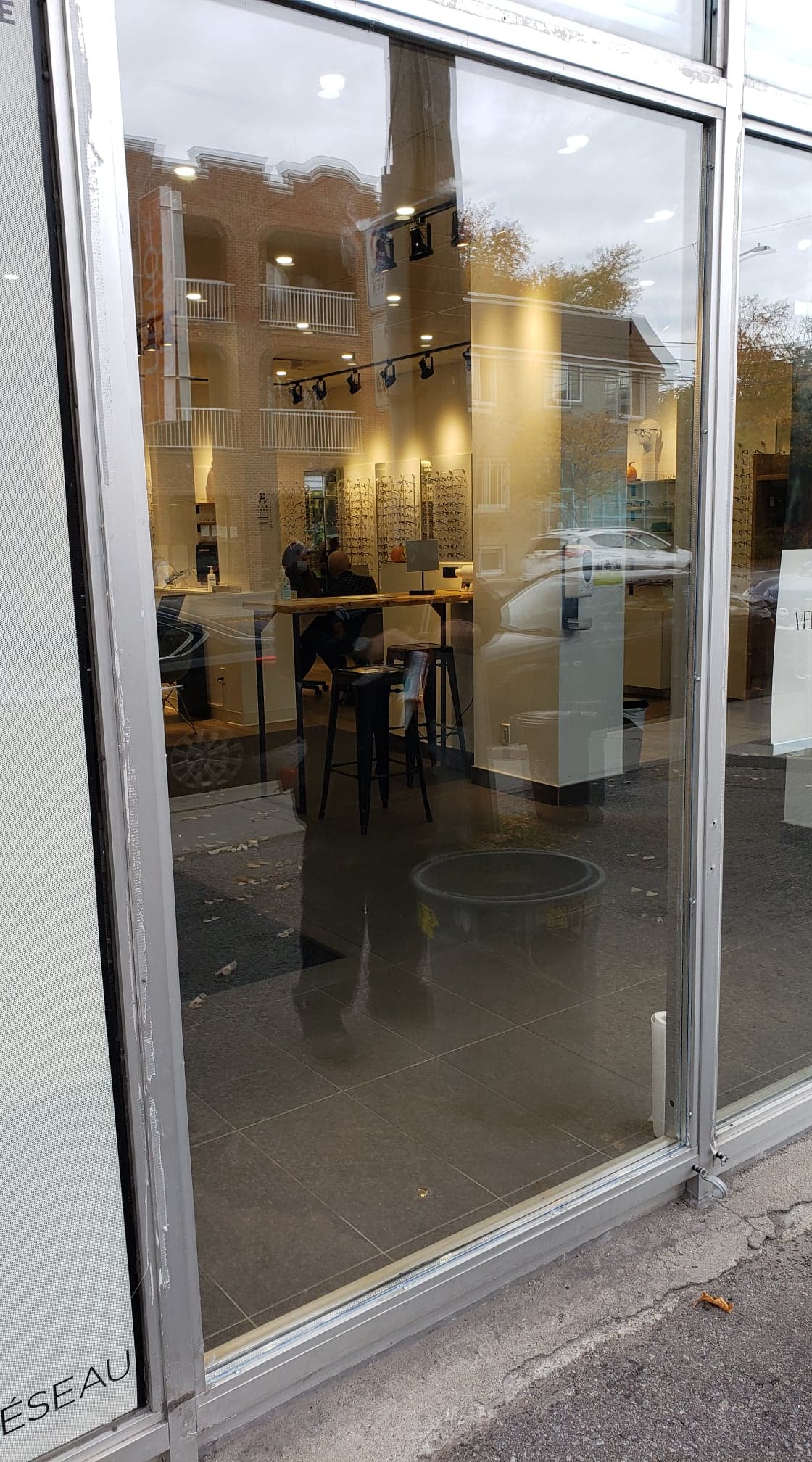 Une façade de magasin avec une porte vitrée et le reflet d'un bâtiment dans la vitre.