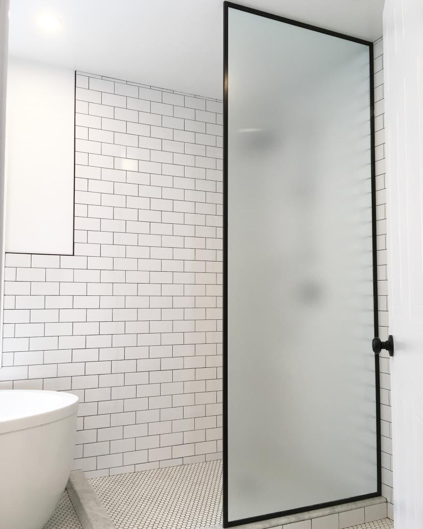 Une salle de bain avec carrelage blanc et une porte de douche en verre