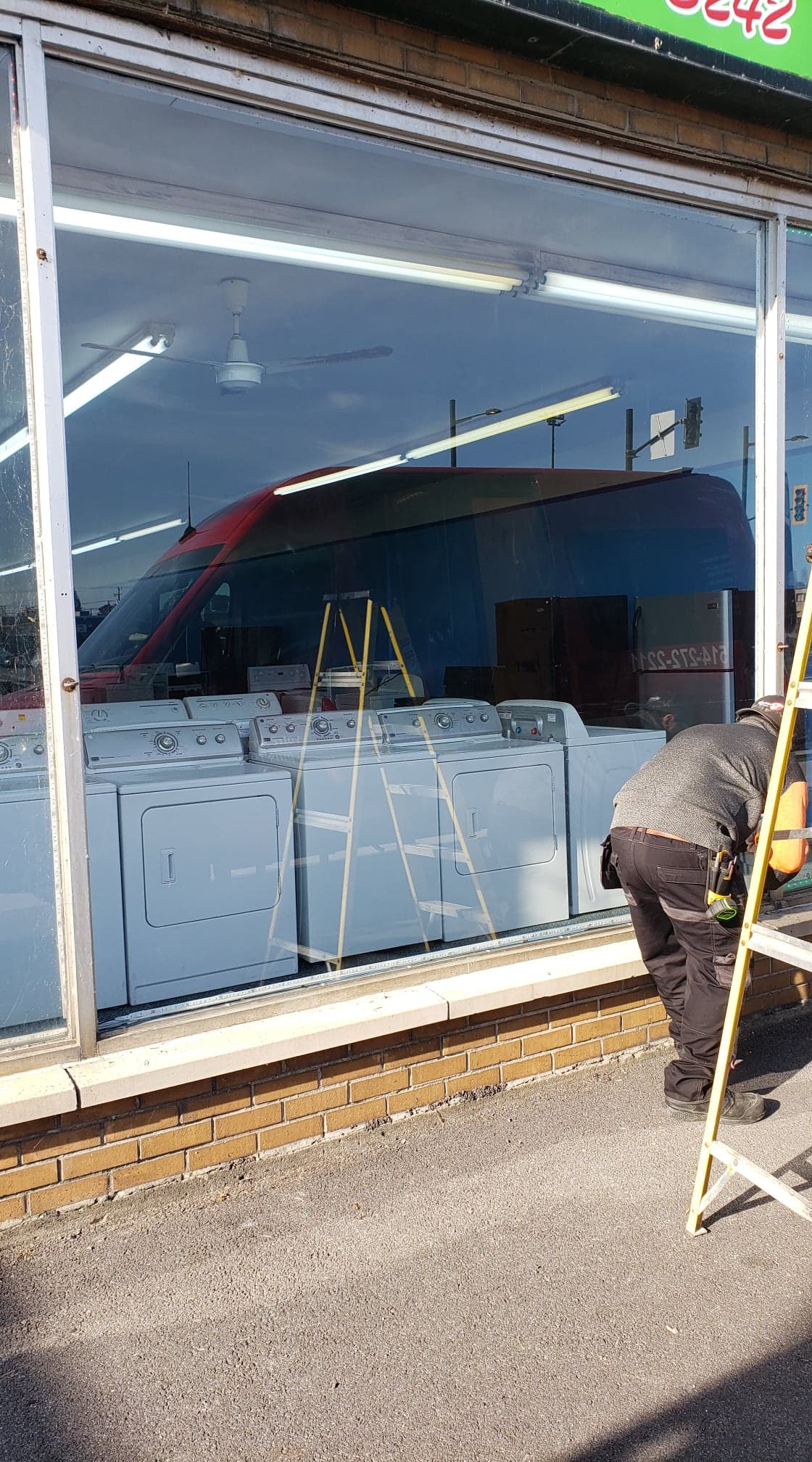 A man is standing on a ladder in front of a store window.