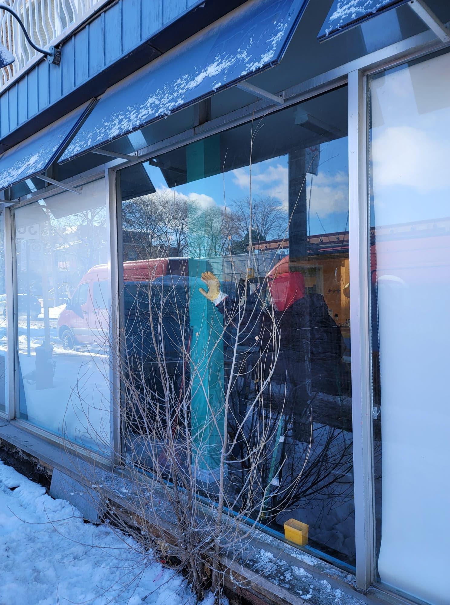 A store front with a blue awning and a reflection of trees in the window