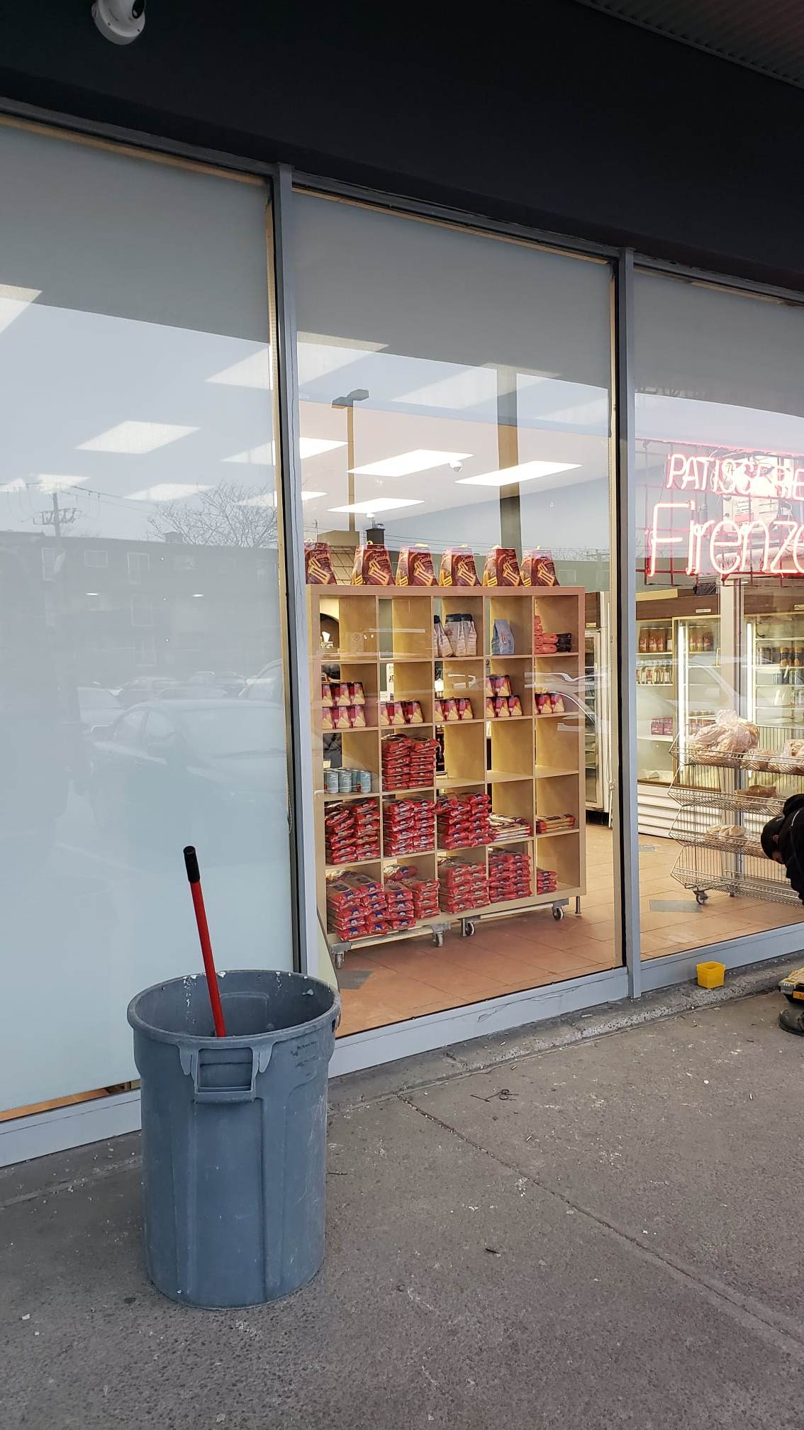 A trash can is sitting in front of a store window.