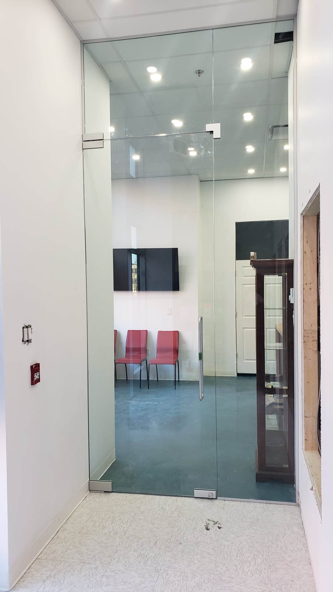 Un couloir avec une porte vitrée menant à une salle d'attente avec des chaises.