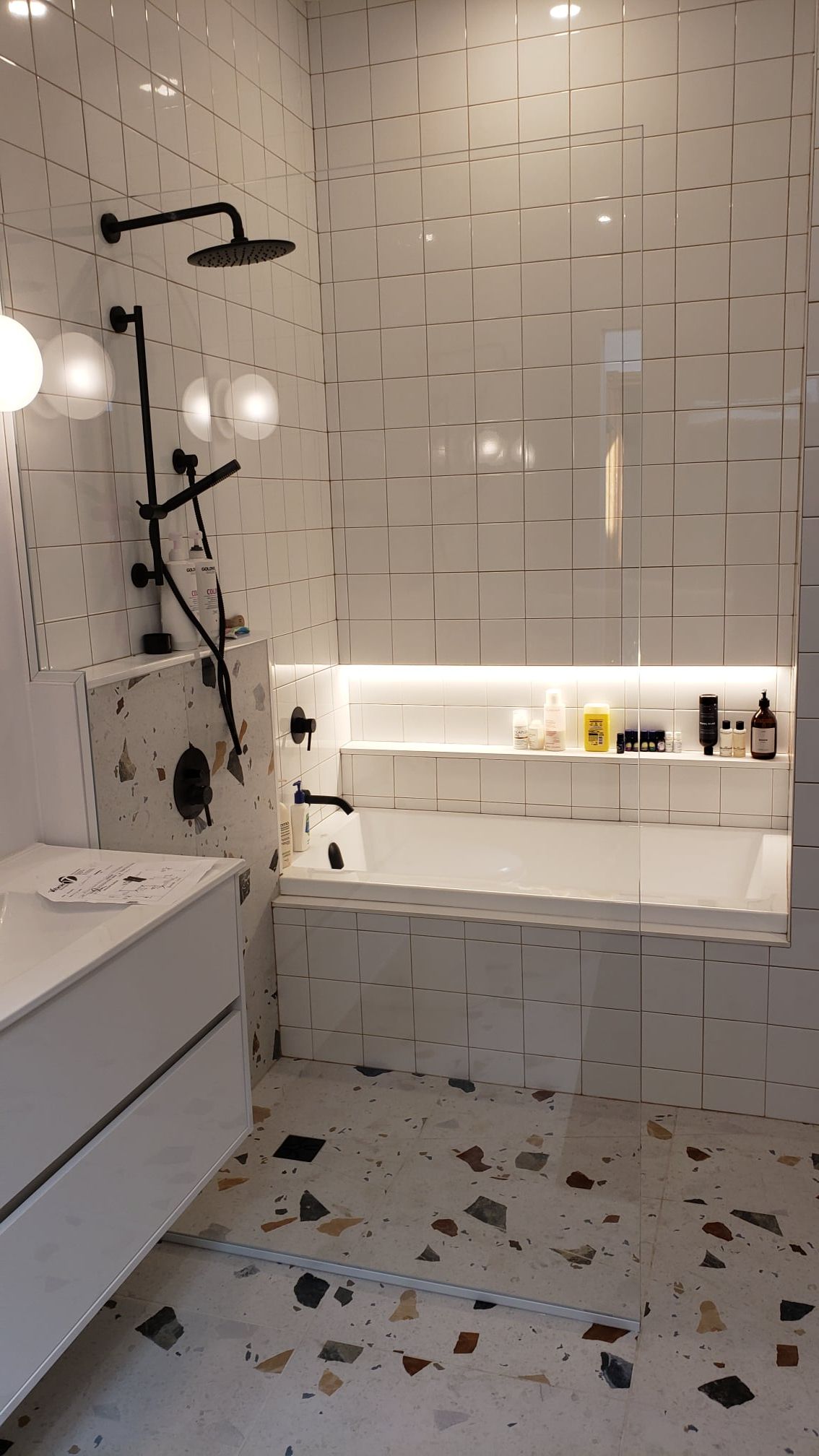 Une salle de bain avec carrelage blanc, une baignoire, une douche et un lavabo.