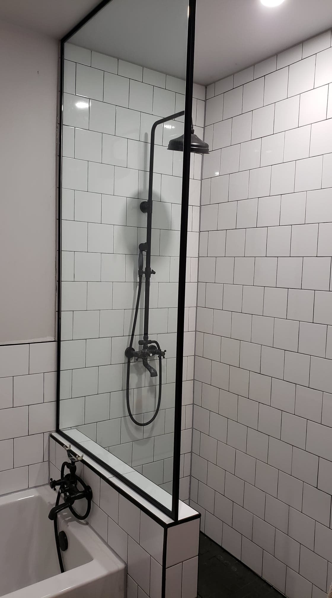 Une salle de bain avec carrelage blanc et une douche avec un cadre noir.