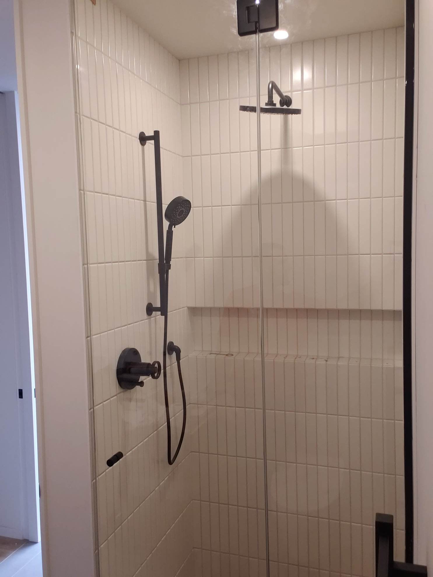 Une douche avec une porte vitrée et une pomme de douche noire.