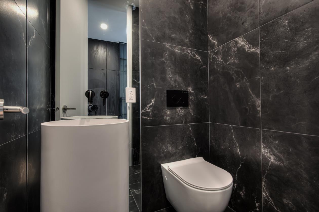 Une salle de bain avec carrelage noir, un WC, un lavabo et un miroir.