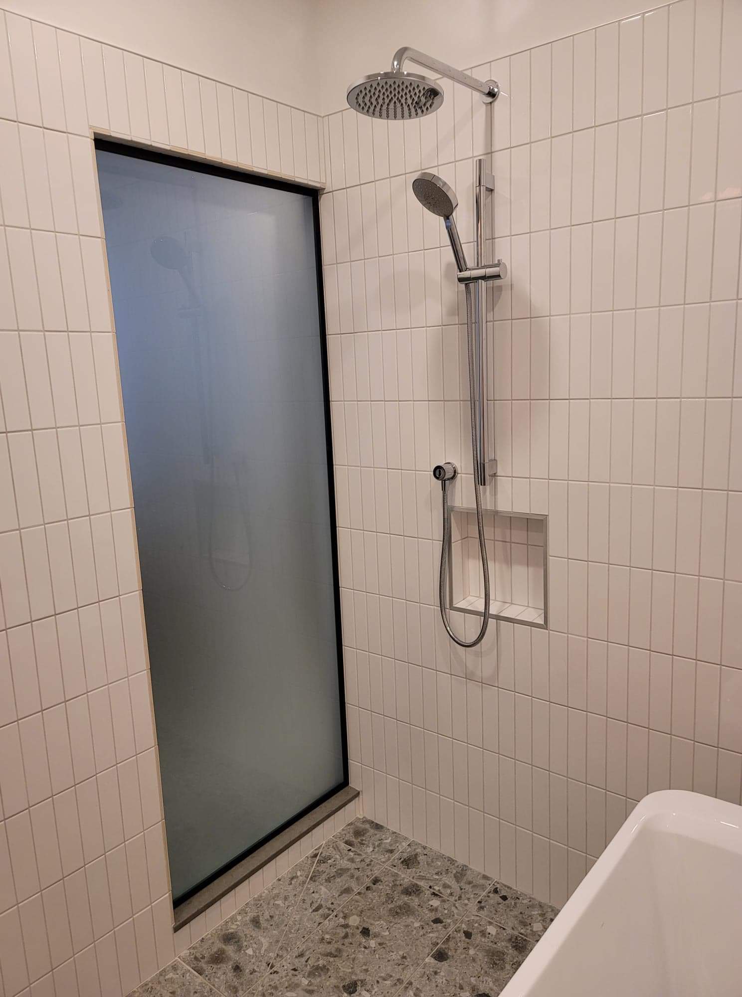 Il y a une douche avec une porte vitrée et un pommeau de douche.