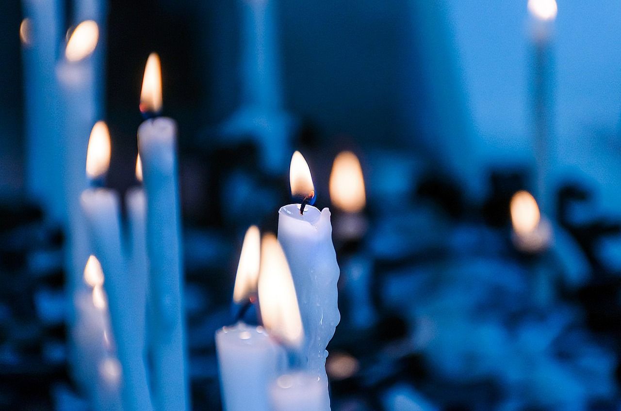 White memorial candles burning with soft flames in a dimly lit remembrance setting