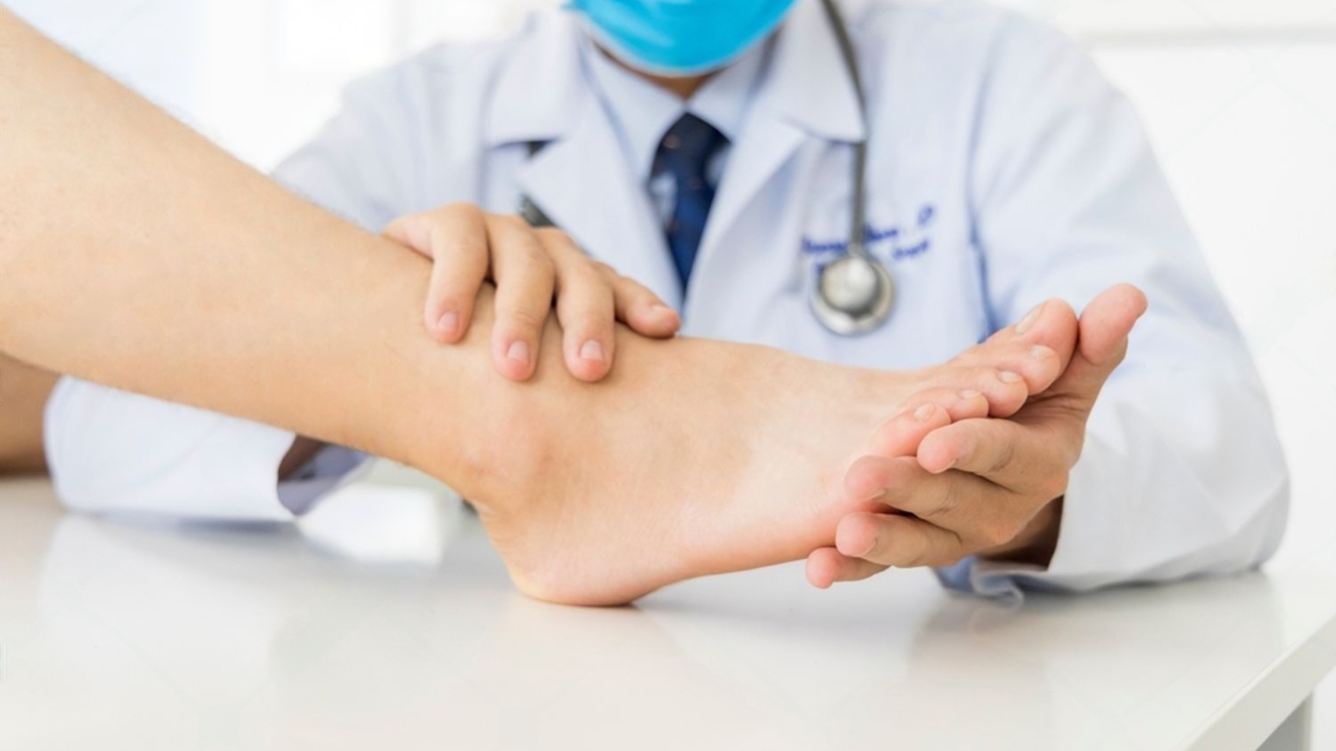A doctor is examining a patient 's ankle while wearing a mask.