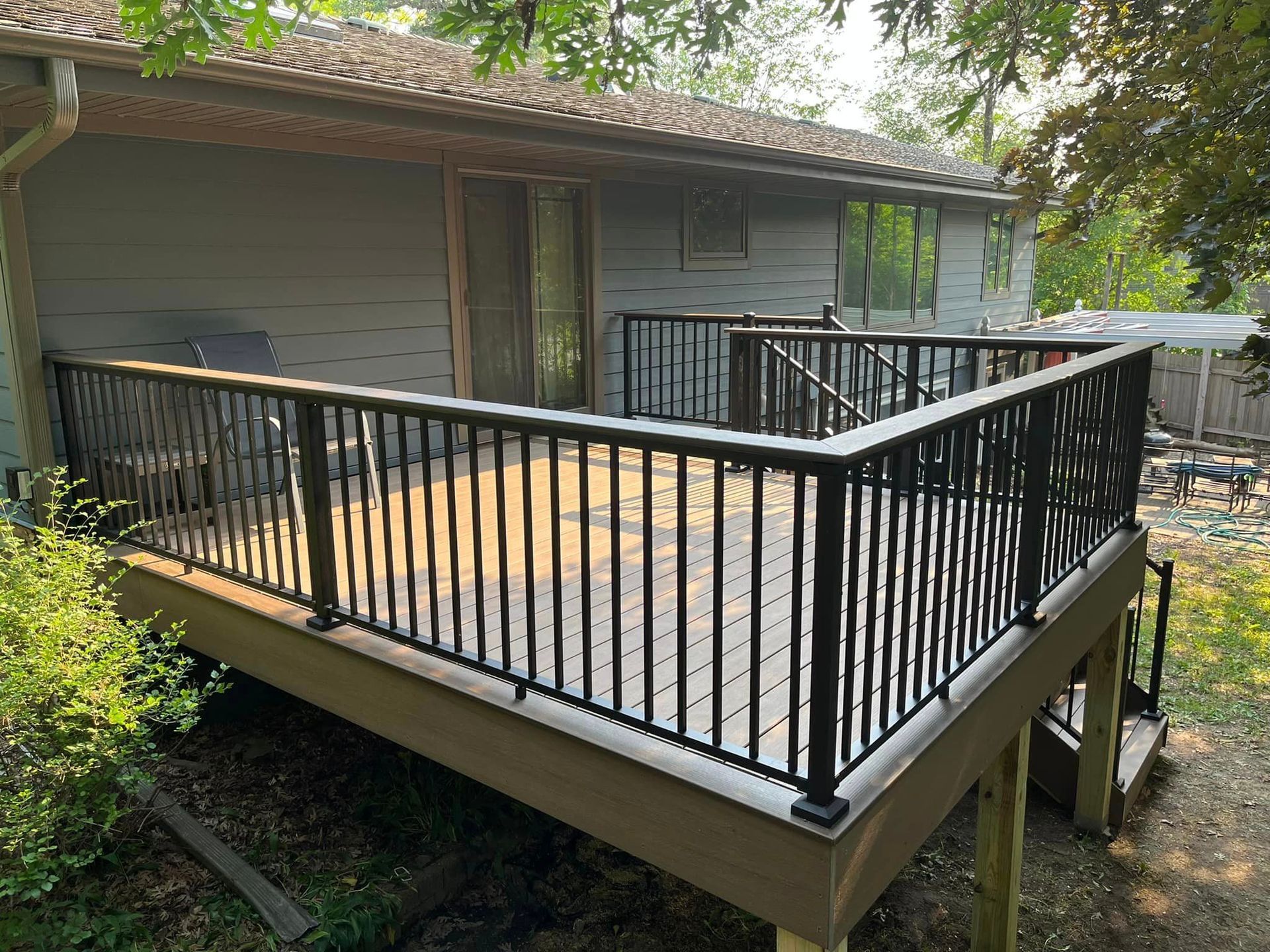A large deck with a black railing is in front of a house.