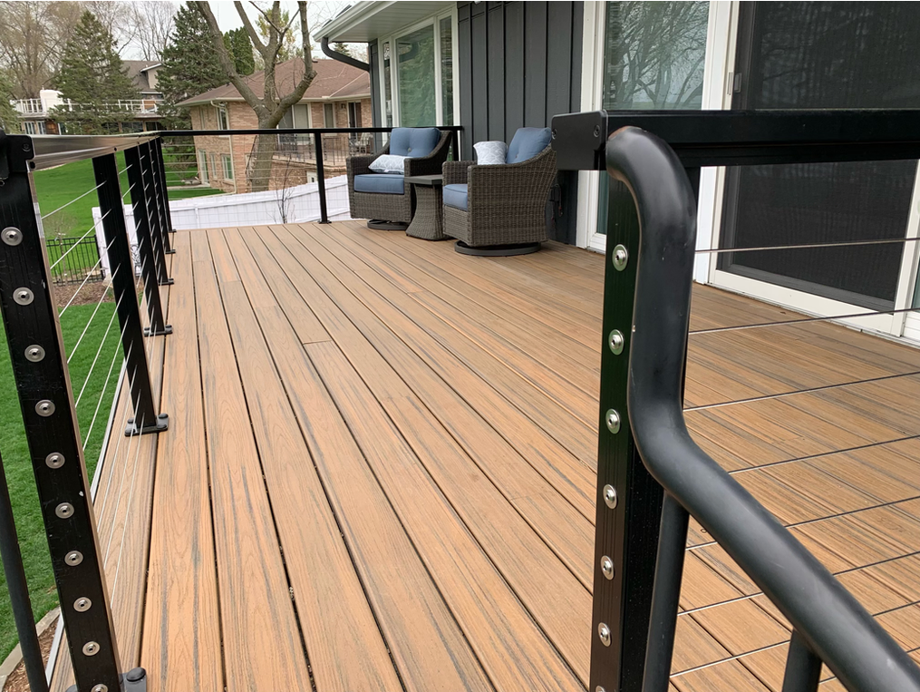 A wooden deck with a black railing and chairs on it.