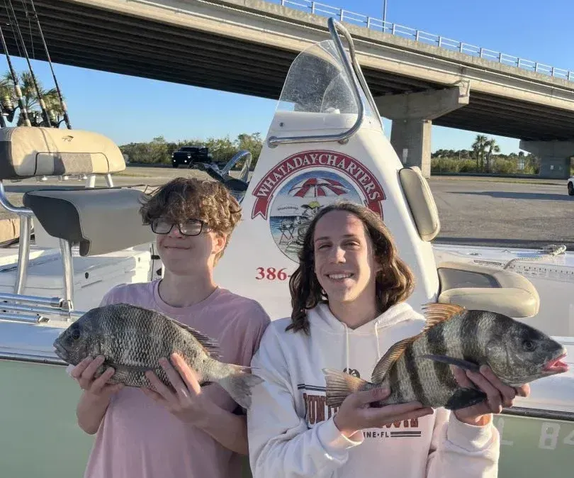 Two people holding fish in front of a boat that says great day charters