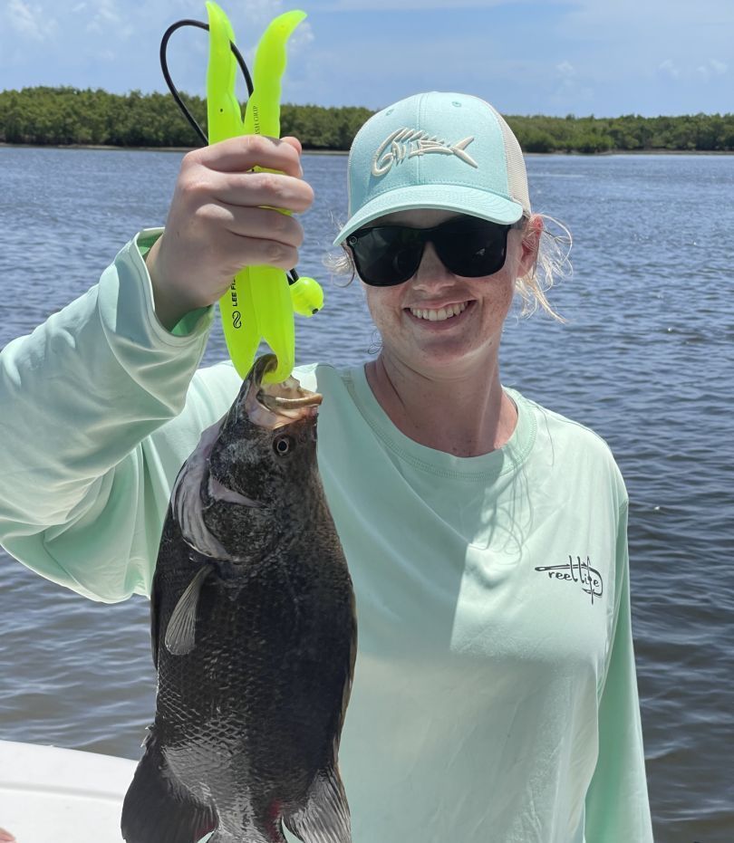 A woman wearing sunglasses and a hat is holding a fish in her hand.