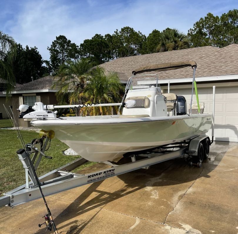 A white boat is parked on a trailer in front of a house