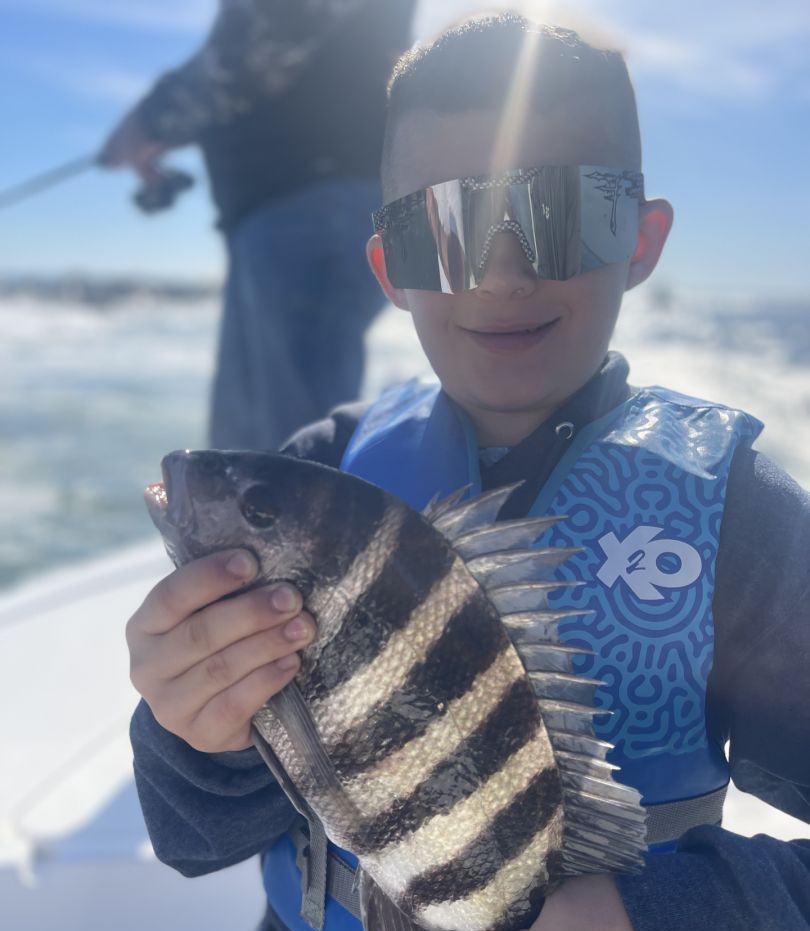 A young boy wearing sunglasses and a life vest is holding a fish