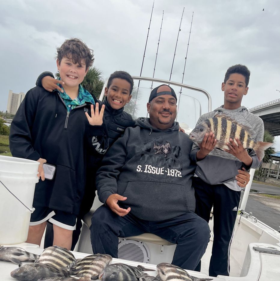 A family on a boat fishing. Father holds a fish, three boys smile. Gray sky, coastal setting.