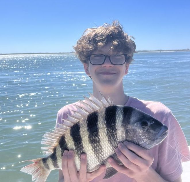 A young man wearing glasses is holding a striped fish in his hands.