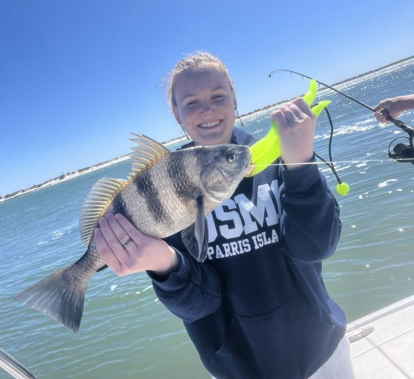 A woman in a parris island sweatshirt is holding a fish