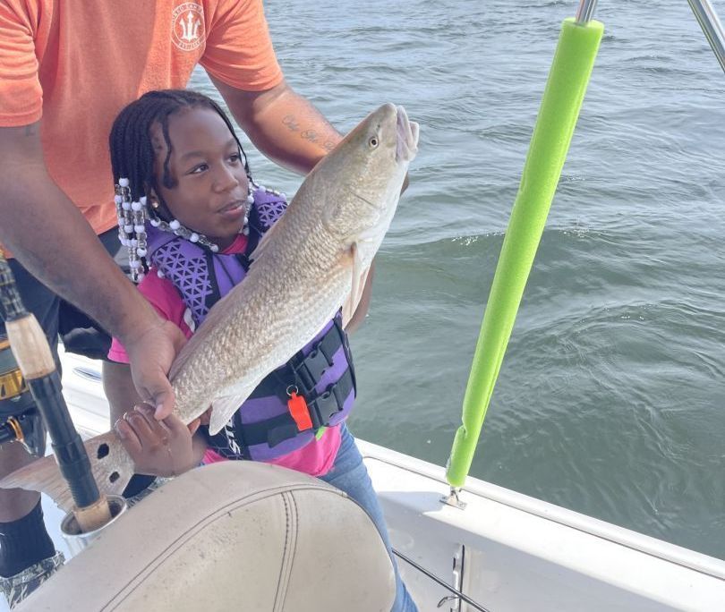 A little girl is holding a large fish on a boat