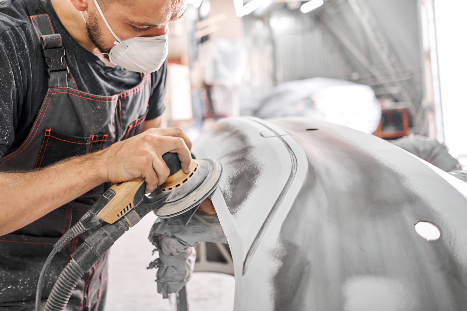 A man wearing a mask is sanding a car with a sander .