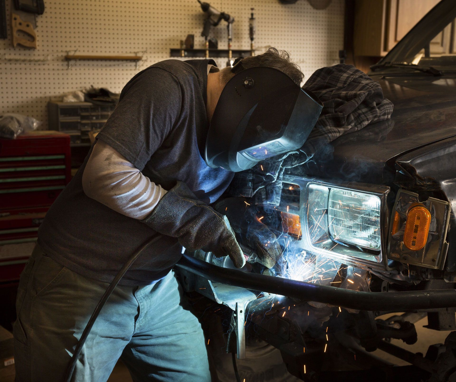 A man wearing a welding mask is working on a car